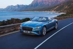 Front side angled view of Continental GTC Azure in Light Windsor Blue driving by the sea